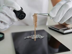 Gold jewelry chain examined with tweezers and a magnifying loupe on a clean work surface.