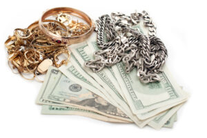 Gold and silver jewelry laid over a stack of U.S. dollar bills on a white surface.
